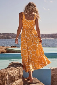 Rear view of a tiered yellow floral midi dress with open back at a sunny beach setting