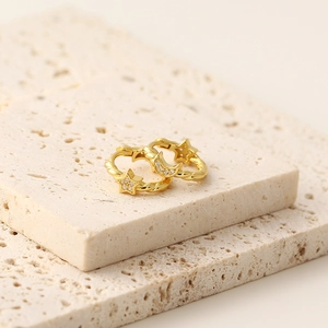 Detail of gold star and moon hoop earrings with small diamonds on beige stone