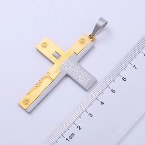 Two-tone stainless steel cross pendant with Spanish scripture next to a ruler for scale