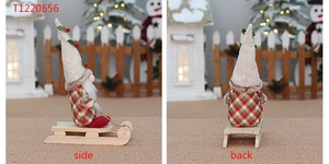Side and back view of fabric Christmas gnome sitting on a wooden sled in snow scene
