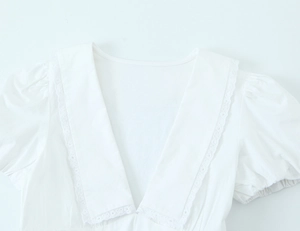 Dettaglio dell'abito in cotone bianco con scollo a V in pizzo e maniche a sbuffo