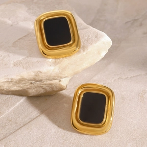 Vintage gold square earrings with black resin inlay on natural stone background
