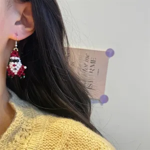 Close-up of handmade beaded Santa Claus earrings worn with a beige cable-knit sweater
