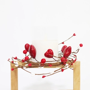 Macro detail of red heart candle ring with festive berries on a wooden stool
