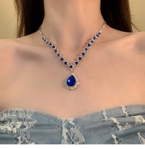 Close-up of luxury silver necklace with teardrop blue gemstone worn by a model