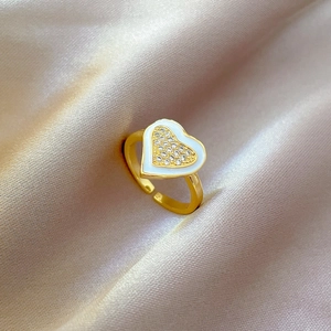 Close-up of golden adjustable heart ring with white enamel and sparkling zircon inlay