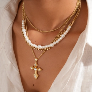 Detail view of multilayer pearl necklace with gold chains and a sparkling cross pendant