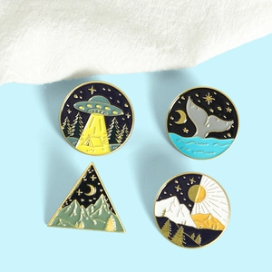 Close-up of four creative enamel pins featuring whale tails and mountain scenery