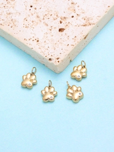 Detail of four golden cat paw pendants with white zircon inlay on a textured beige stone