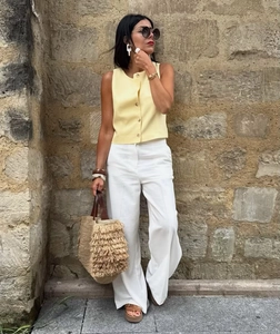 Detail of casual yellow sleeveless linen top paired with white wide-leg trousers on model
