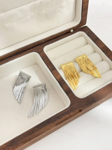 Detail of gold and silver tassel earrings resting in a premium wooden jewelry box