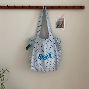 Light blue polka dot canvas tote bag with 'Beach' print hanging on a wooden hook