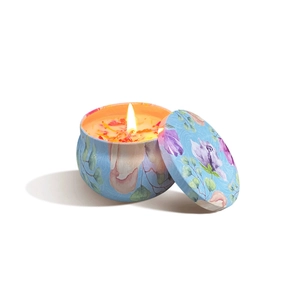 Blue floral patterned scented candle in tin with lit flame and dried flower petals