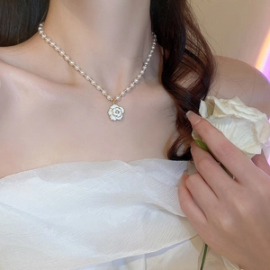 Close-up of elegant pearl necklace featuring a white camellia pendant with gold edging