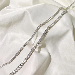 Macro view of silver tennis chain with round cubic zirconia on white satin fabric