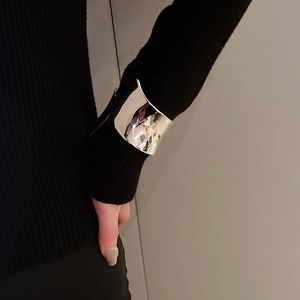 Dettaglio di un largo bracciale a polsino in argento lucido sopra una manica di maglia