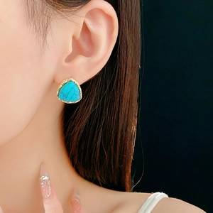 Close-up of a vintage triangle turquoise earring with gold frame worn by a model