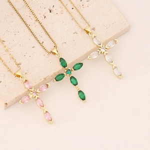 Three gold cross necklaces with pink, green, and clear marquise zircons on textured stone