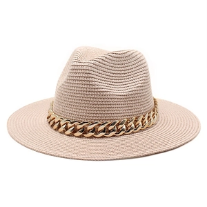 Detail of khaki straw fedora hat featuring a chunky gold acrylic chain band on top