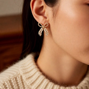 Close-up of bow knot earrings with gold plating and zircons on a model's ear