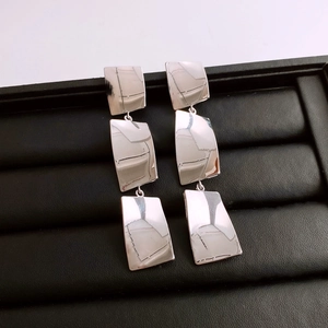 Macro shot of silver metallic triple square geometric drop earrings on black display