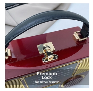 Macro shot of gold metal clasp and radio dial detail on wine red acrylic clutch