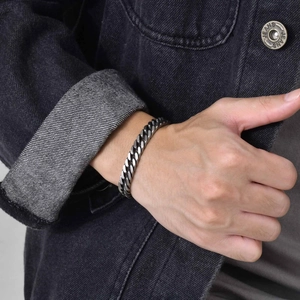 Detailed view of silver stainless steel Cuban link bracelet on a male wrist with denim jacket