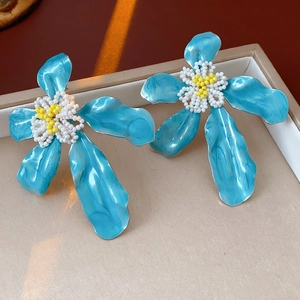 Vue macro de boucles d'oreilles fleurs en émail bleu dans une boîte à bijoux beige