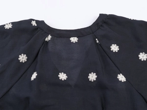 Close-up of black V-neck bodice with white floral embroidery and pleated puff sleeve detail
