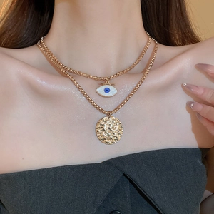Detail view of a double-layered gold necklace with evil eye and hammered coin charms