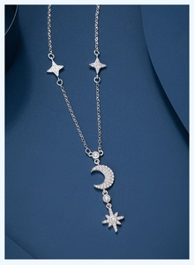 Detail of silver star and moon necklace with sparkling zircon tassel on dark blue background
