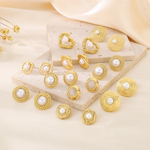 Detailed macro view of assorted gold pearl stud earrings on a textured stone surface