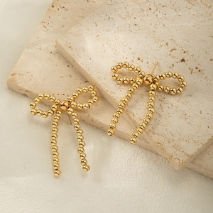 Detail of gold bow earrings with beaded tassels on an elegant marble background
