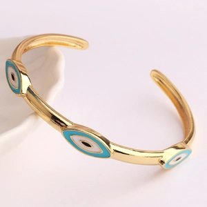 Golden C-shaped open bracelet with blue and black enamel evil eye charms on white