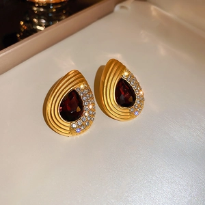 Close-up of golden teardrop earrings with a red gemstone and crystal inlay detailing