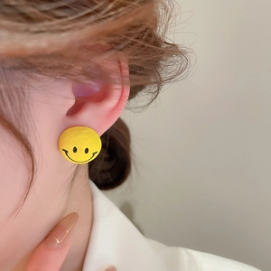 Close-up of model wearing cute yellow smiley face stud earrings in a minimalist style