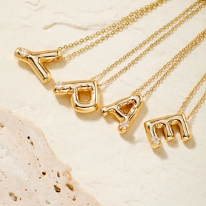 Golden 3D bubble alphabet necklaces with zircon stones on natural stone background