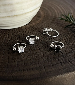 Close-up of four silver ear cuffs with clear and black gemstones on a wooden slice