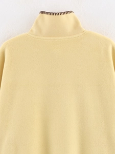 Detail shot of soft yellow fleece texture with brown stitched edges on a cloak collar