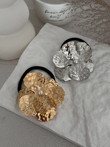 Detailed view of flower-shaped hair ties in gold and silver with pearl centers on paper