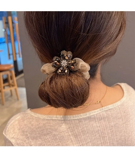 Detail of a sparkling rhinestone clover hair tie on a golden champagne organza scrunchie