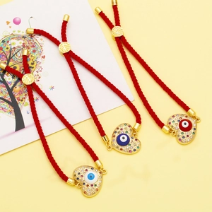Red cord heart bracelet with evil eye design and gold plating on beige background