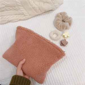 Detailed view of a soft pink lamb wool cosmetic bag with a fuzzy hair tie and floral clip
