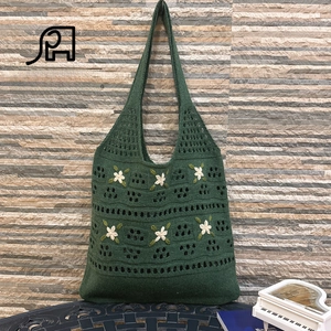 Close-up of dark green crochet tote bag with white flower embroidery and knit texture