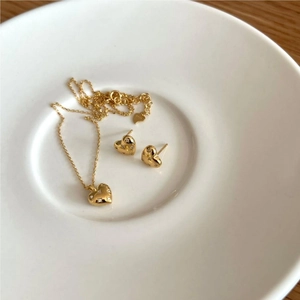 Macro detail of gold heart pendant and stud earrings set with sparkling zircons on ceramic
