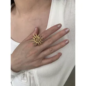 Detailed view of a gold sun-shaped ring with textured spiral center on a model's hand