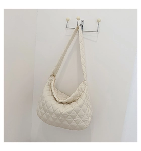 Detailed view of white quilted tote bag with wide strap hanging on wall hook