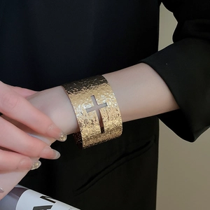 Détail d'un large bracelet doré martelé avec croix ajourée sur fond de costume noir