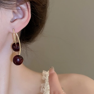 Close-up of deep red resin cherry earrings with gold stems worn on a model's ear