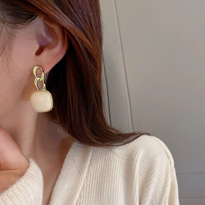 Boucles d'oreilles carrées blanc crème avec chaîne dorée portées par un mannequin